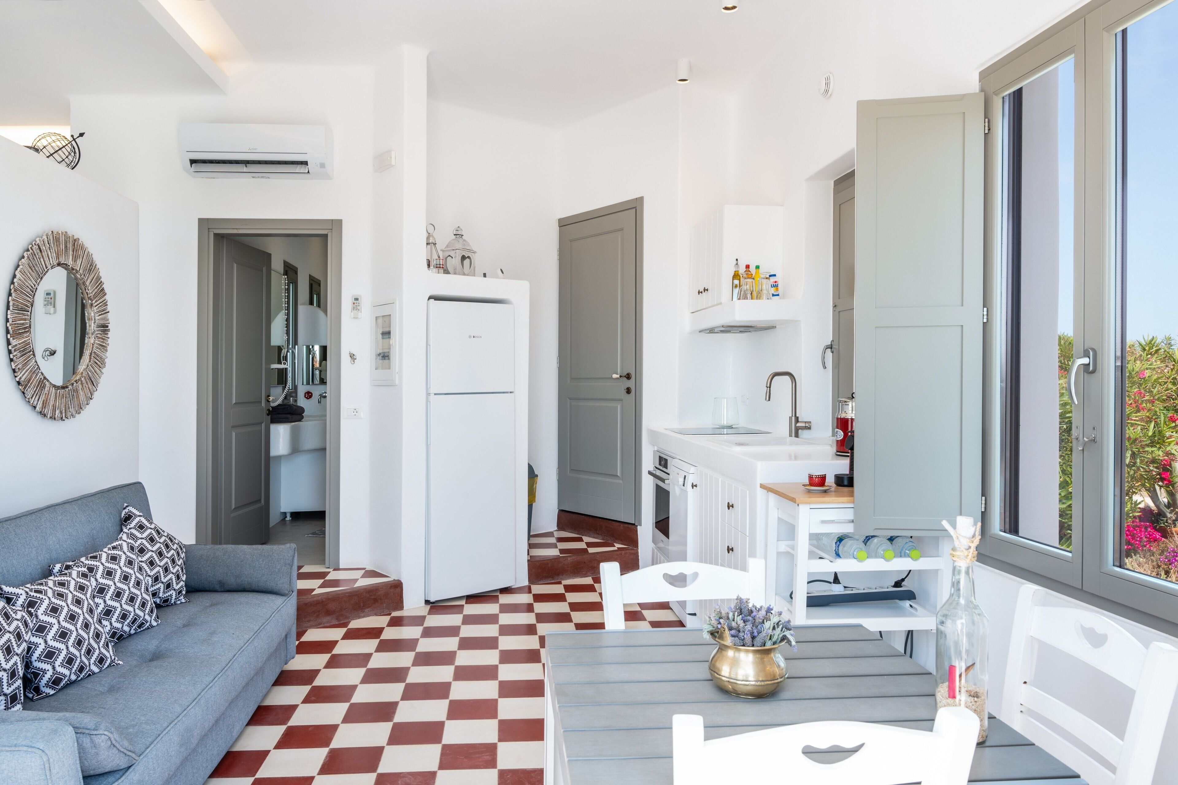 Un ambiente compatto con pavimento a scacchi, un divano, un tavolo da pranzo, una cucina con mobili bianchi e un'ampia finestra.