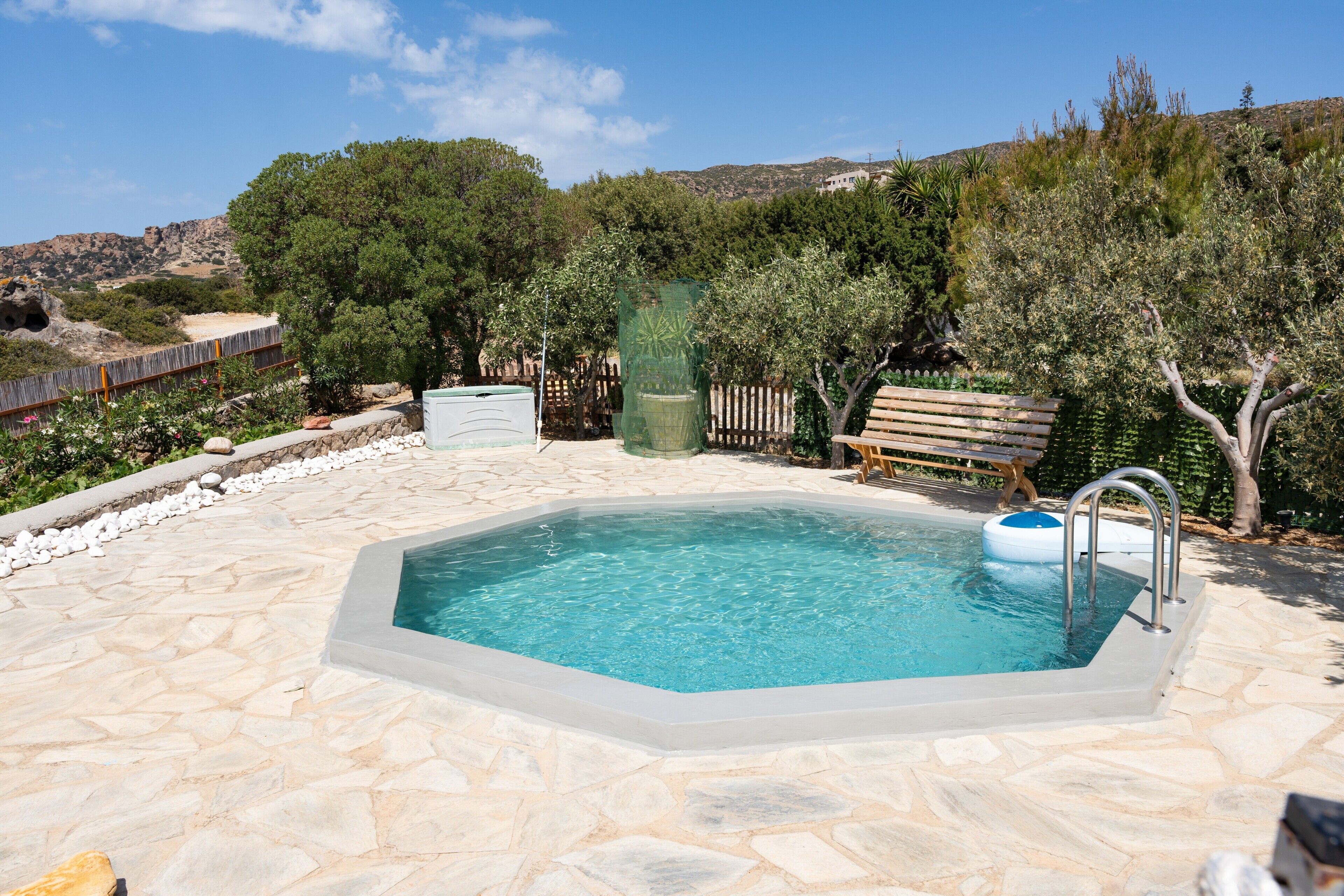 Une piscine aux bords recouverts de pierres, entourée d’arbres et délimitée par une clôture en bois.