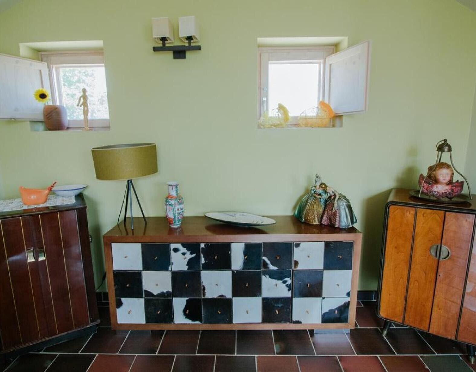 Una habitación con un aparador a cuadros, una lámpara, un jarrón y un estante pequeño con adornos.
