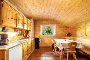 A wooden cabin interior with a kitchen, dining area, and a window with a view of greenery. - Holiday Apartment 'Almbergerhof Wohnung Hirzer' with Mountain View and Balcony (San Martino In Passiria)