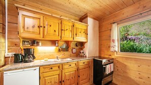 Cocina estilo cabaña de madera con armarios de madera, un lavamanos, un lavavajillas, una estufa y una ventana con vistas a zonas verdes.