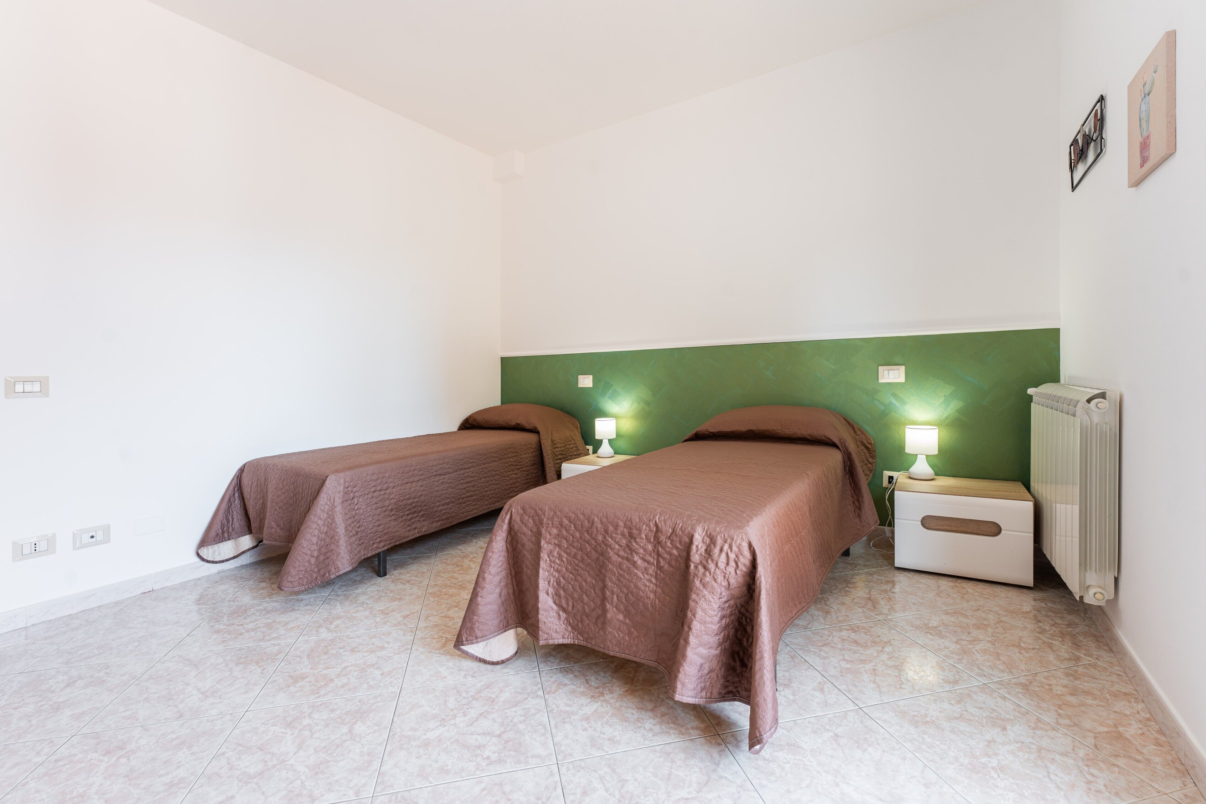 Habitació amb dos llits, una paret d'accent verd, un radiador i una tauleta de nit amb una làmpada.