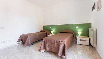 Habitació amb dos llits, una paret d'accent verd, un radiador i una tauleta de nit amb una làmpada.