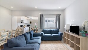 Una sala de estar moderna con sofá, mueble para TV y un comedor con sillas y mesa.