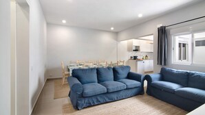 Una sala moderna con un sofá azul, una mesa de comedor con sillas, y una cocina al fondo.