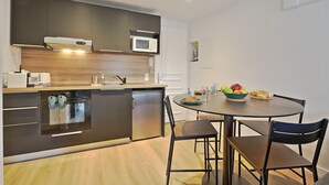 Una cocina moderna con armarios oscuros, un microondas empotrado y un horno de acero inoxidable. Hay una mesa de comedor con sillas y un tazón de fruta.