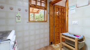 Uma cozinha com janela, porta de madeira, paredes com azulejos e uma pequena mesa de madeira com uma cesta.