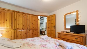 Quarto com armários de madeira, uma cama com roupa de cama floral, uma televisão em uma cômoda de madeira e um espelho com iluminação.