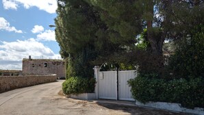 Uma entrada com portão, um muro de pedra, e um edifício ao fundo.