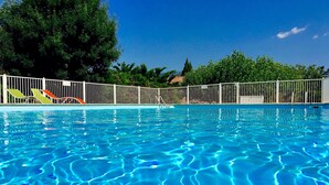 Ein Schwimmbecken mit klarem, blauem Wasser, umgeben von einem weißen Zaun und Bäumen im Hintergrund.