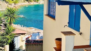 Ein Küstengebäude mit einer Treppe, die zu einem Balkon führt, mit Blick auf das klare, blaue Meer und üppiges Grün.