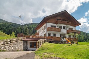 Un grand bâtiment à deux étages doté d’un balcon en bois, d’une petite structure attenante et d’une aire de jeux avec un toboggan.