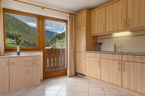 A kitchen with wooden cabinets, a window with a view of mountains, and a rose on the windowsill. - Apartment 'Wohnung 1' with Mountain View, Shared Garden and Wi-Fi (Sarentino)