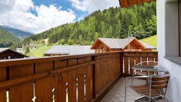 A wooden balcony with a table and chairs, overlooking a forested mountain area.