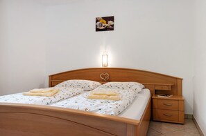 Ein ordentlich bezogenes Bett mit Blumenmuster, ein Nachttisch mit Schubladen, eine Wandleuchte und ein kleines Bild über dem Bett.