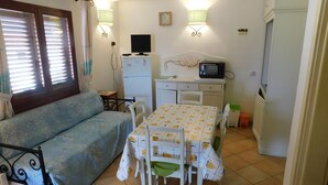 Un espace de vie compact comprenant un canapé, une table à manger, des chaises, un téléviseur, un réfrigérateur et un four à micro-ondes.