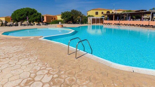Une piscine entourée d’une terrasse en pierre, de chaises longues et d’un espace abrité avec des parasols.