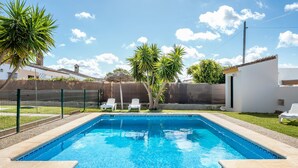 Une piscine rectangulaire à l’eau d’un bleu limpide, bordée d’une margelle en pierre. Deux chaises longues blanches sont disposées au bord de la piscine.