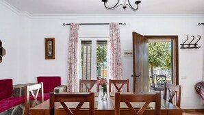 Un coin repas avec une table et des chaises en bois, un canapé rouge et une porte donnant sur l’extérieur.