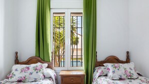 Une chambre avec deux lits, une table de chevet en bois et une fenêtre ornée de rideaux verts.