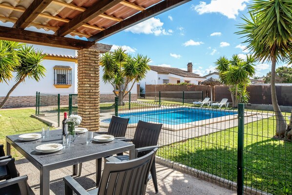 Une terrasse avec une table dressée pour les repas, une piscine et un jardin clos.