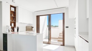 Una cuina moderna amb una illa central, prestatges de fusta i una porta corredissa de vidre que dona a un balcó.