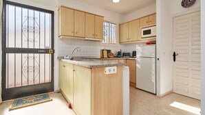 Una cocina compacta con armarios de madera, microondas integrado, refrigerador y pileta.
