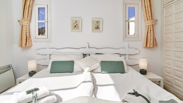 Un dormitorio con cabecera blanca, dos mesitas de noche con lámparas, cama con ropa de cama blanca y almohadas verdes, y dos cuadros en la pared.