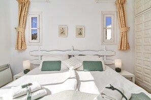 A bedroom with a white headboard, two bedside tables with lamps, a bed with white bedding and green pillows, and two framed pictures on the wall.