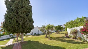 Una zona residencial con un sendero pavimentado, un alto árbol perenne y un edificio blanco con techo de tejas.