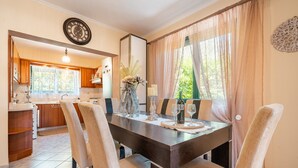 A dining area with a dark wooden table, beige chairs, a vase with dried plants, and a clock on the wall.
