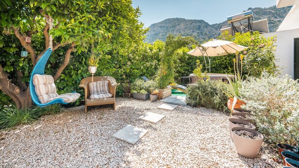 A patio with a swing chair, a cushioned chair, potted plants, and a view of a mountain.