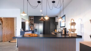 Una cuina moderna amb una illa central, il·luminació penjant i una paret d'accent de fusta.
