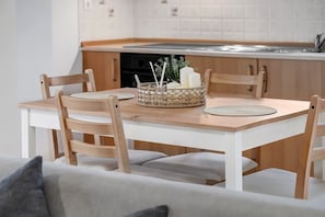 En matplats med ett träbord, fyra stolar, en flätad korg med ljus och ett kök i bakgrunden.