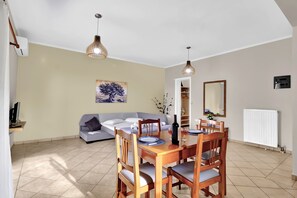 A dining area with a wooden table and chairs, a sofa, a painting on the wall, and a radiator.
