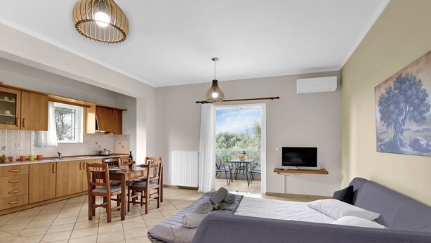 A modern kitchen with wooden cabinets, a dining area with a table and chairs, a large bed with pillows, and a TV on the wall. - Apartment 'Elaia  2' with Sea View, Wi-Fi and Air Conditioning (?e???da)