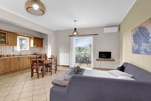 A modern kitchen with wooden cabinets, a dining area with a table and chairs, a large bed with pillows, and a TV on the wall.
