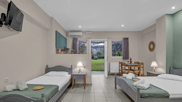 A hotel room with two beds, a TV, a table with chairs, and a view of the outdoors. - Studio Apartment 'Elaia  3' with Mountain View, Wi-Fi and Air Conditioning (?e???da)