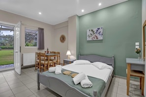 A hotel room with a bed, a desk, a chair, a window with curtains, a wall clock, and a painting.