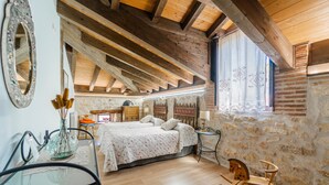 Un dormitorio con techo de madera, una cama con colcha estampada, una mecedora y una pared de piedra.
