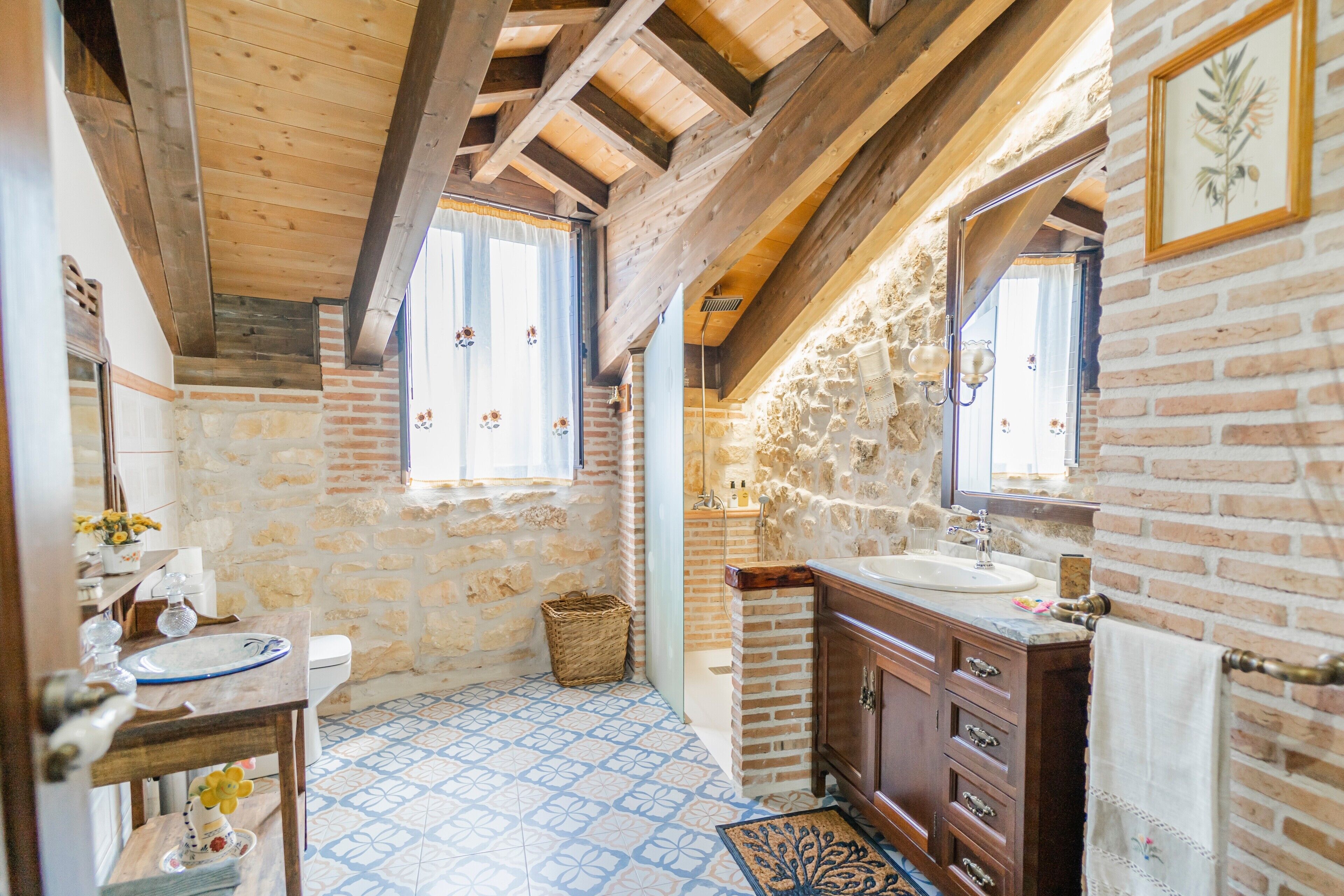 A rustic bathroom with exposed wooden beams, a stone wall, a sink, and a mirror.