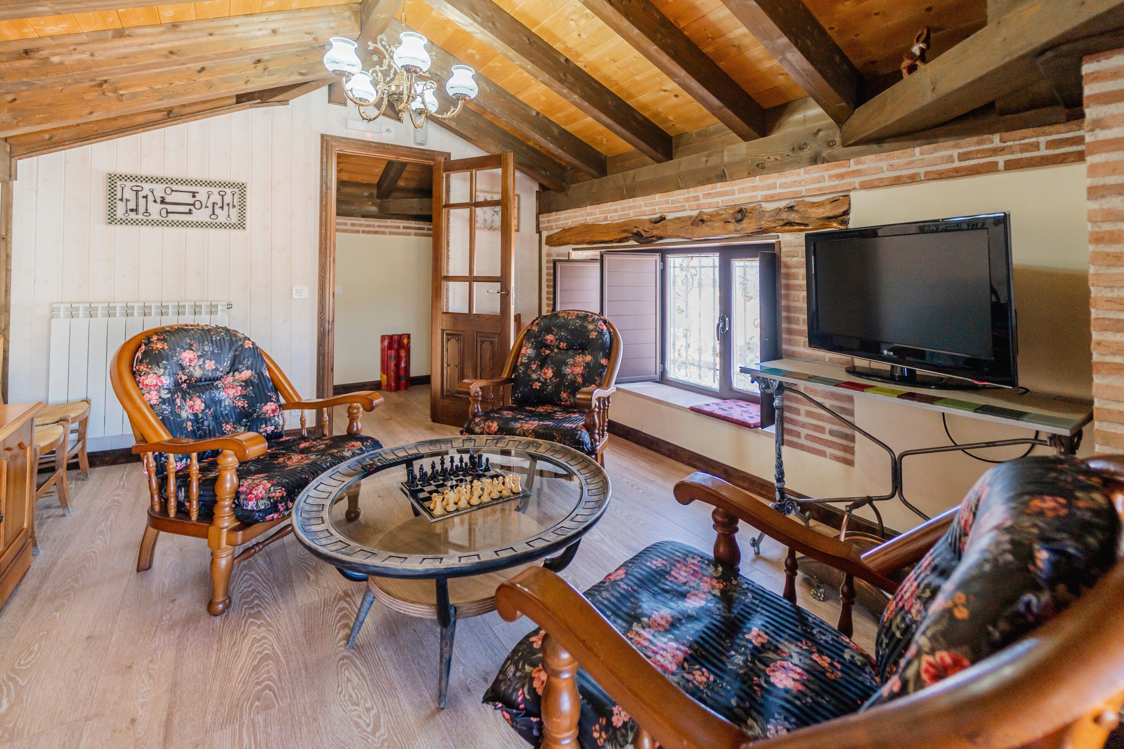 A cozy room with wooden beams, a fireplace, a television, and a chess table.