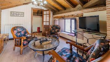A cozy room with wooden beams, a fireplace, a television, and a chess table.