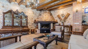 Una chimenea de piedra con un estufa de leña moderna, un mueble de madera con puertas de cristal y una araña.