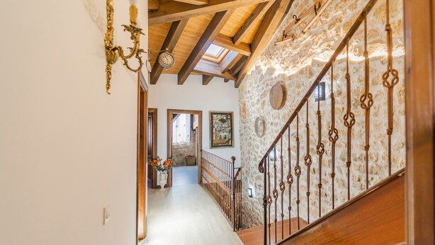 Un pasillo con una escalera de madera, paredes de piedra y un candelabro.