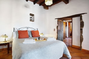 Een slaapkamer met een bed, kussens, een dienblad met ontbijtartikelen, een nachtkastje, een lamp en een stenen muur.
