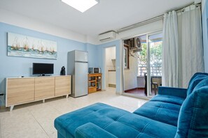 A living room with a blue sofa, a TV, a refrigerator, and a painting of sailboats on the wall.