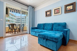 A blue sofa in a room with a sliding glass door leading to an outdoor area with a table and chairs.