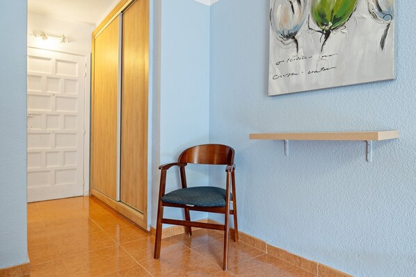 A hallway with a wooden door, a chair, and a wall-mounted shelf.