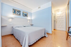 A bedroom with a bed, a wall-mounted shelf, and a door leading to another room.